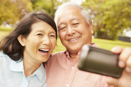 Older Asian couple smiling confidently because they were both able to get new dentures from the restorative dentistry services at Sound to Mountain Dental in Tacoma, WA.