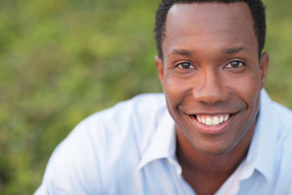 Man looking at the camera and smiling without being able to tell has a dental bridge to correct his smile. 