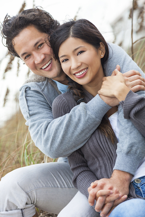 Attractive Asian couple sitting, hugging and smiling over the smile makeovers they received with the help from Dr. Hickey from Sound to Mountain Dental in Tacoma, WA.